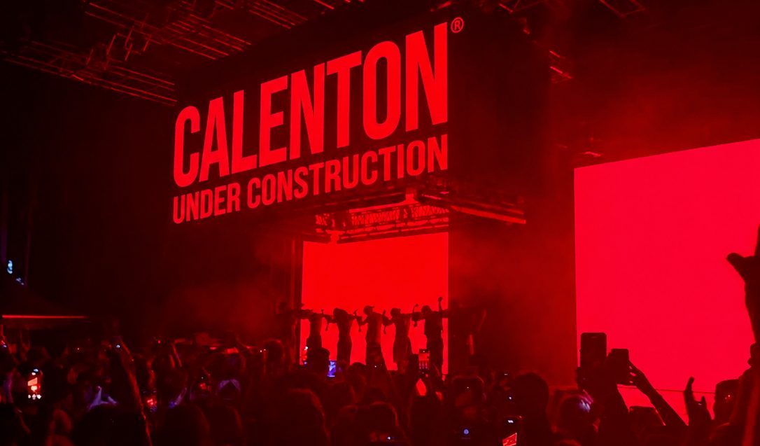 A packed dark room with the stage screen glowing red.